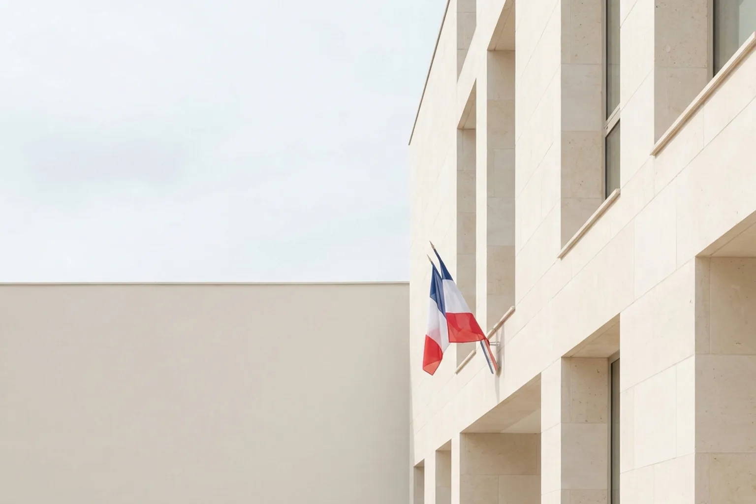 Façade de pierre claire d'une mairie française en plein jour, drapeau tricolore discret