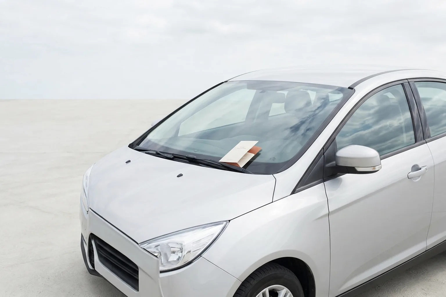 Imprimé plié glissé sous l'essuie-glace d'une voiture claire, ciel couvert lumineux reflété dans le pare-brise
